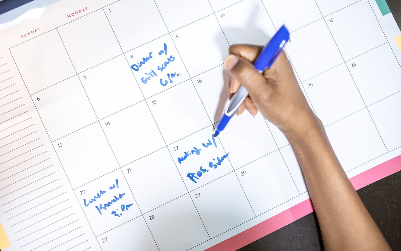 Mano anotando citas a lápiz sobre un calendario de papel, casilla por casilla.