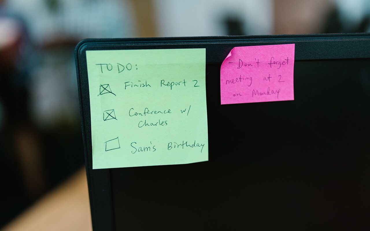 Notas adhesivas con recordatorios escritos a mano pegadas al borde de un monitor.